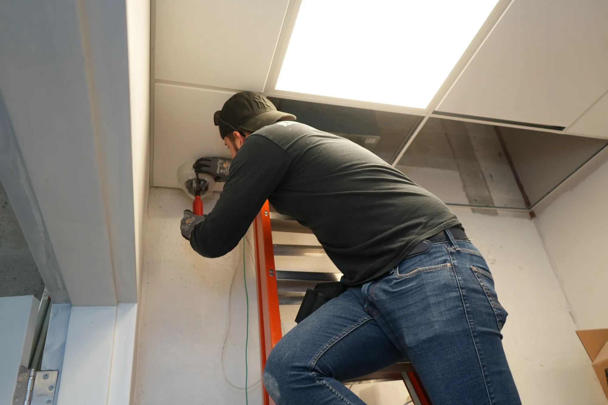 DIST technician on a ladder servicing a ceiling-mounted camera